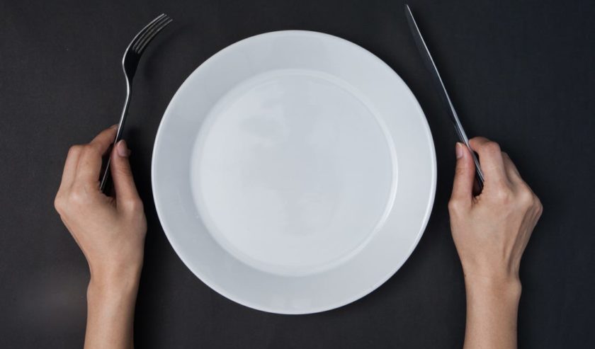 Orang memegang sendok dan garpu dengan piring kosong