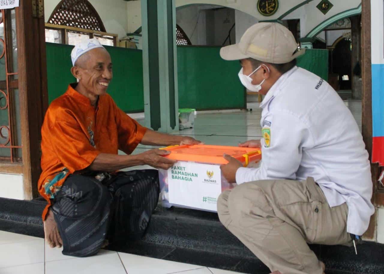seorang laki-laki menerima paket bantuan dari baznas di sebuah masjid