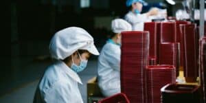 beberapa orang pekerja menyelesaikan pekerjaan di pabrik menghadapi wadah plastik berwarna merah