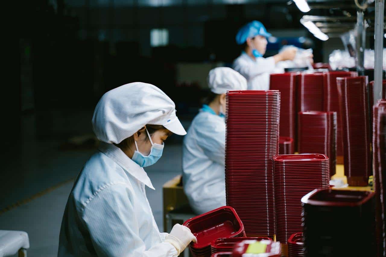 beberapa orang pekerja menyelesaikan pekerjaan di pabrik menghadapi wadah plastik berwarna merah